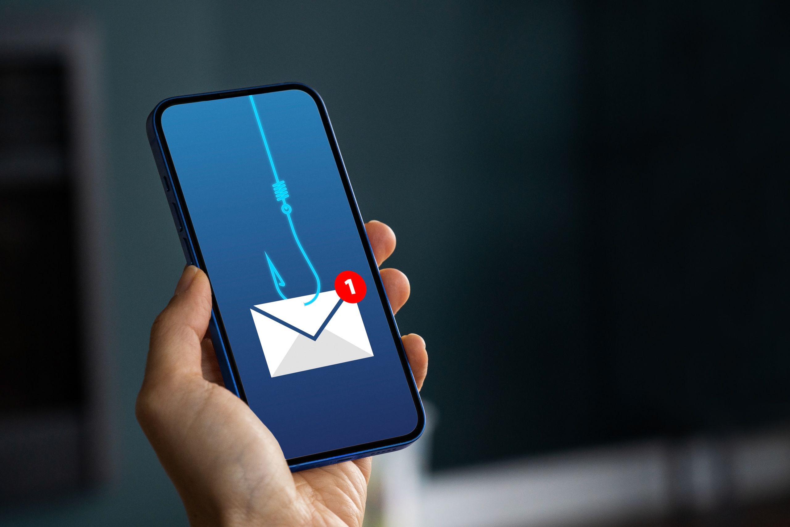 hand holding a cell phone. On the screen is an envelope held by a hook.