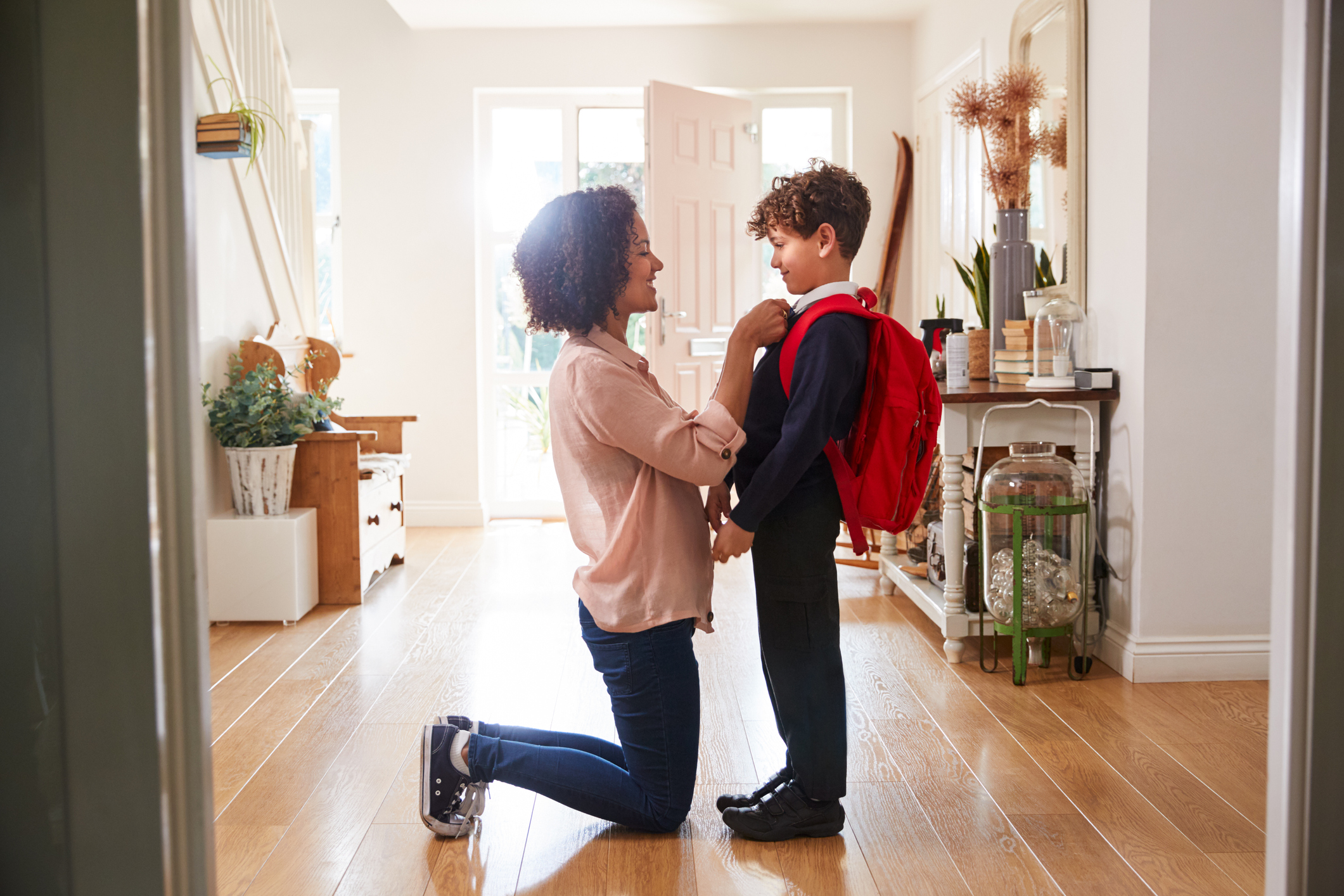 A mother on her knees preparing her young son in uniform to leave for school